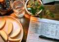 Glass of Water Beside Slices of Apple and Record on Calorie Count on Brown Wooden Table