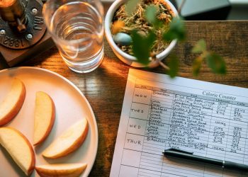 Glass of Water Beside Slices of Apple and Record on Calorie Count on Brown Wooden Table