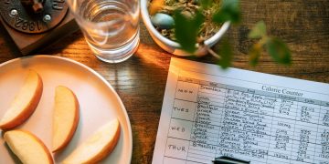 Glass of Water Beside Slices of Apple and Record on Calorie Count on Brown Wooden Table