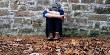 Boy Sitting on Ground Leaning Against Brickstone Wall