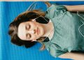 Tranquil woman resting on yoga mat in earphones at home