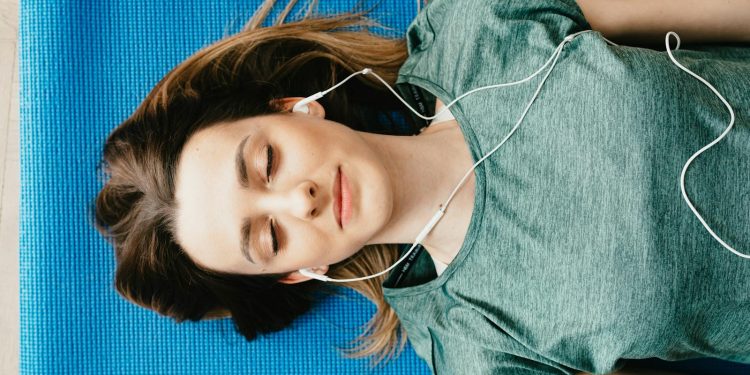Tranquil woman resting on yoga mat in earphones at home
