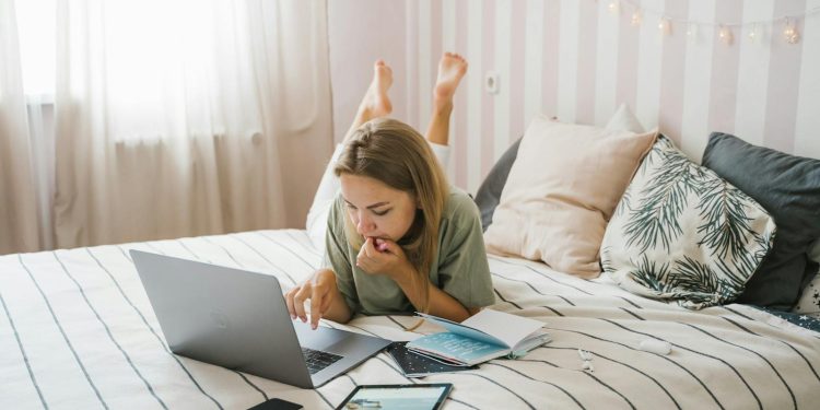 Woman Lying on Bed While Using a Laptop