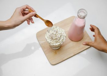 People taking dessert and glass bottle of milkshake placed on wooden board