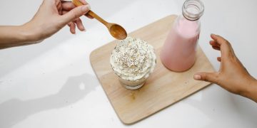 People taking dessert and glass bottle of milkshake placed on wooden board