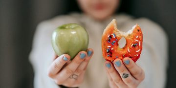 Woman showing apple and bitten doughnut
