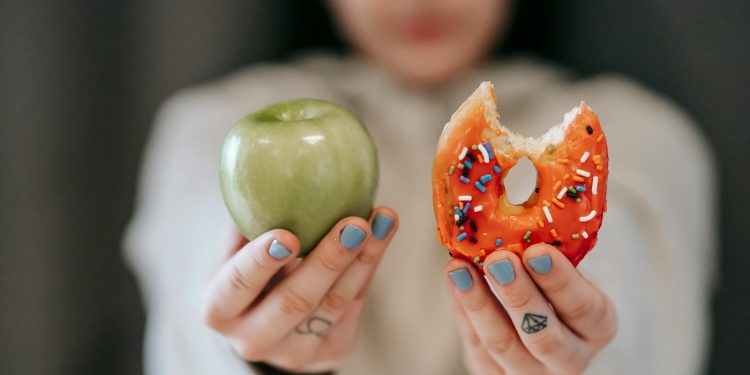 Woman showing apple and bitten doughnut