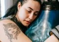 Tired young lady leaning on punching bag after boxing training