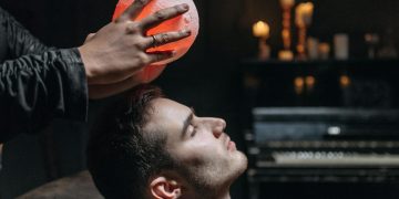 Person Holding an Illuminated Round Object on a Man's Forehead