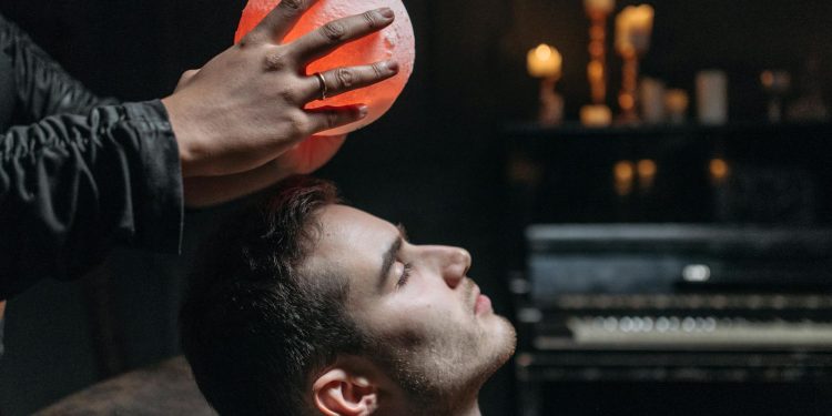 Person Holding an Illuminated Round Object on a Man's Forehead