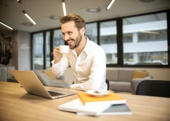 Depth of Field Photo of Man Sitting on Chair While Holding Cup in Front of Table
