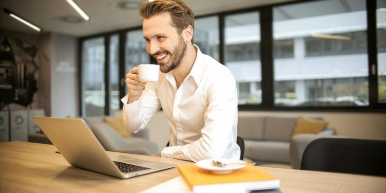Depth of Field Photo of Man Sitting on Chair While Holding Cup in Front of Table